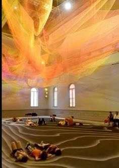 people are laying on the floor in a large room with colorful fabric hanging from the ceiling