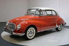 an old red and white car is parked in a room with a black round floor