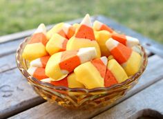 a glass bowl filled with candy cornucons on top of a wooden table outside