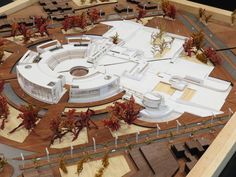 a model of a circular building with trees around it and buildings on the other side