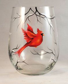 a wine glass with a red bird painted on the side and branches around it, in front of a white background