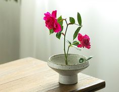 a white bowl with pink flowers in it sitting on a wooden table next to a potted plant