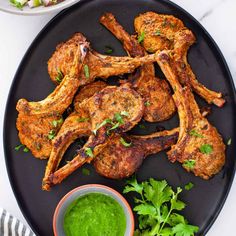 some chicken wings on a black plate with green sauce and garnished parsley