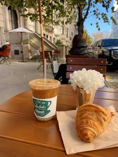 a croissant and coffee sit on a table in front of a sidewalk cafe