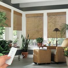 a hand holding a remote control in front of a living room window with bamboo blinds