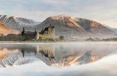 a castle sitting on top of a lake surrounded by mountains