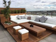 an outdoor seating area with white cushions and wooden furniture on top of a roof deck