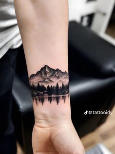 a person with a tattoo on their arm holding up a small mountain and forest scene