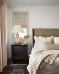 a bedroom with a bed, nightstand and lamp on the side table in front of it