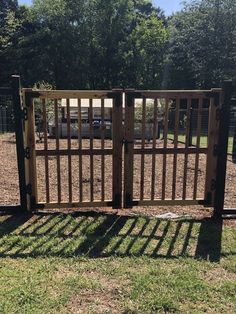 an open wooden gate in the middle of a grassy area with trees and grass behind it