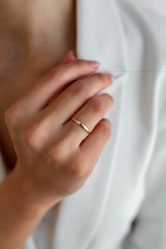 a woman's hand with a gold ring on her left wrist and the other hand holding an object in front of her chest