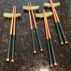 five green and gold colored chopsticks laying on top of a counter