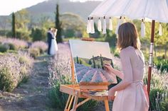 a woman in a pink dress is painting lavenders on an easel with a white umbrella