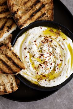 a bowl of hummus and grilled bread on a black plate with olive oil