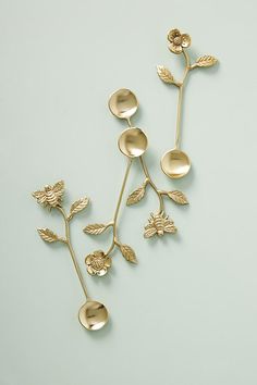 two metal spoons with leaves and flowers attached to each other on a white surface