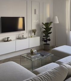 a living room filled with white furniture and a flat screen tv mounted on the wall