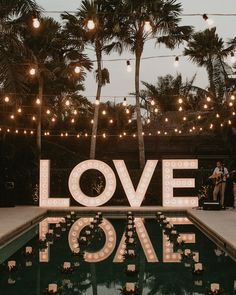 a sign that says love is in front of some palm trees and lights hanging from the ceiling