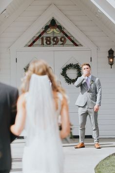 a man standing in front of a white building next to a woman wearing a wedding dress