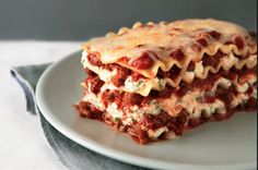 a white plate topped with lasagna covered in sauce and cheese next to a fork