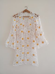 white crochet top with yellow flowers hanging on a hanger against a wall