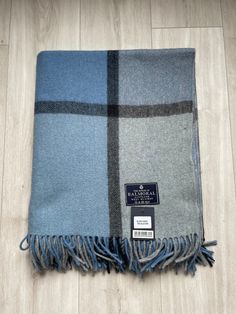 the blue and grey plaid scarf is laying on top of a wooden floor with a tag