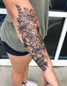 a woman's arm with flowers on it and a black ink tattoo that is in the shape of a flower