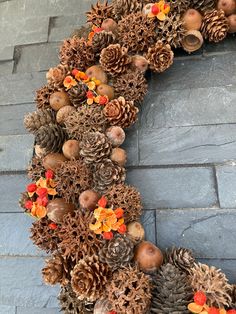 a wreath made out of pine cones and acorns on a stone wall with autumn decorations