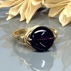 "Smooth Amethyst Gemstone Round Ring - Sterling Silver, 14k Yellow or Rose Gold Filled Wire Wrapped- Custom Size (full, .25, .5, .75) MATERIALS: ❀  This natural round amethyst gemstone wire wrapped ring is handmade with an approximately 10mm bead and your choice of wire.   You will receive the stone pictured for your ring. SIZING: ❀  This ring (as well as all the others in my shop) is custom made to any size from 4 to 14 including half and quarter sizes!  DIRECTIONS FOR CHECKOUT To checkout, please select the SIZE of the ring and your choice of BAND COLOR/WIRE from the drop down menus.     Band Color MEANINGS on the Drop down menu; Silver Tone, Gunmetal Tone, Rose Gold Tone, Yellow Gold Tone Wire- This is Craft wire (please see below for more details)   Silver- Solid Argentium Sterling Sil Adjustable Gold Amethyst Ring Gift, Adjustable Gold Amethyst Birthstone Ring, Hand Wrapped Round Purple Jewelry, Hand Wrapped Purple Round Jewelry, Wire Wrapped Ring, Color Meanings, Argentium Silver, Wire Wrapped Rings, Round Rings