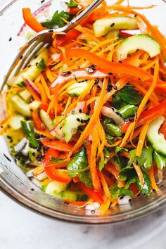 a salad with carrots, cucumbers and other vegetables in a glass bowl