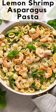 lemon shrimp asparagus pasta in a white bowl with basil leaves and lemon wedges on the side