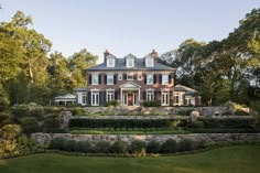 a large brick house surrounded by trees and bushes in front of a lush green lawn