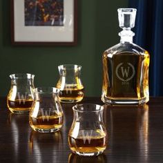 four whiskey glasses sitting on a table next to a decanter with the letter w in it