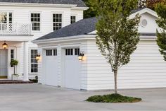 a large white house with two garages and trees in front of the entrance to it