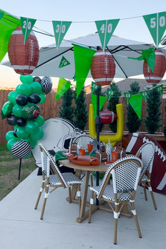 an outdoor table and chairs with football decorations on the top, along with balloons in the shape of footballs