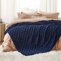 a bed with a blue blanket on top of it next to pillows and a window