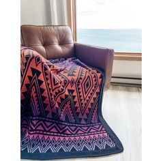 an orange and purple blanket sitting on top of a brown chair next to a window