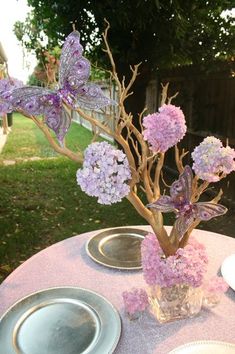 purple flowers are in a vase on top of a table with plates and silverware