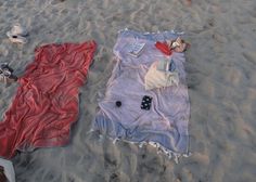 two blankets are laying on the sand at the beach, one has a remote control