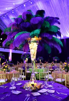 a tall vase filled with purple flowers next to a table covered in plates and silverware