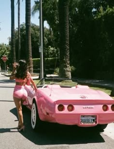 a woman in pink is leaning on the hood of a pink car