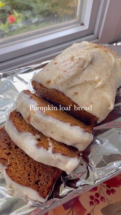 three slices of pumpkin loaf bread with frosting on top, sitting on aluminum foil in front of a window