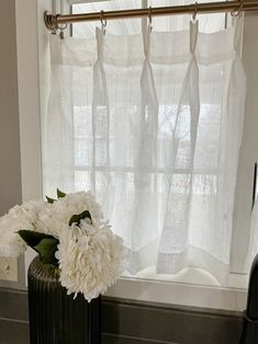 a vase with white flowers sitting on a window sill in front of a curtain