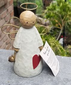 a ceramic angel figurine holding a heart with a note attached to it's back