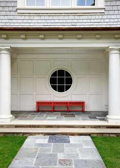 a red bench sitting in front of a white building with columns and a round window