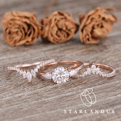 three wedding rings on top of a wooden table next to some dried flowers and cones