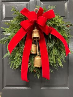 a christmas wreath hanging on the front door with a bell and red ribbon tied around it