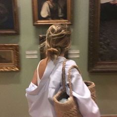 a woman carrying a wicker basket in front of paintings