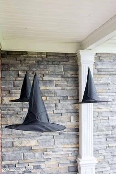 two black witches hats hanging from the side of a brick wall next to a white column