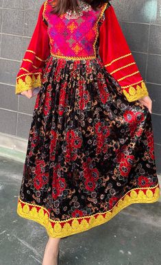 This vibrant traditional dress showcases a bold pink handmade top with colorful square patterns and long red sleeves edged with golden details. The black skirt is patterned with red and grey flowers, highlighted by a bright yellow hemline featuring gold floral designs. This dress combines simplicity with elegance, making it perfect for cultural events or as a unique addition to any collection for those who appreciate a touch of tradition. Red Long Sleeve Dress With Traditional Patterns, Red Long Sleeve Dresses With Traditional Patterns, Red Traditional Drape Dress With Embroidered Border, Traditional Red Dress With Embroidered Border, Red Dress With Embroidered Border In Traditional Drape, Red Bohemian Dress For Transition Seasons, Bohemian Red Dress For Seasonal Wear, Red Dresses With Traditional Patterns For Festivals, Red Dresses With Embroidered Border For Traditional Ceremonies