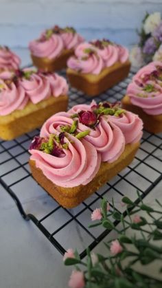 some pink frosted pastries are on a cooling rack with flowers in the background